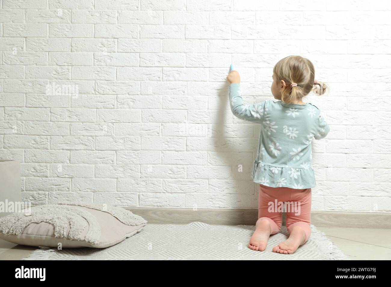 Little girl drawing on white brick wall indoors, back view and space for text. Child`s art Stock Photo